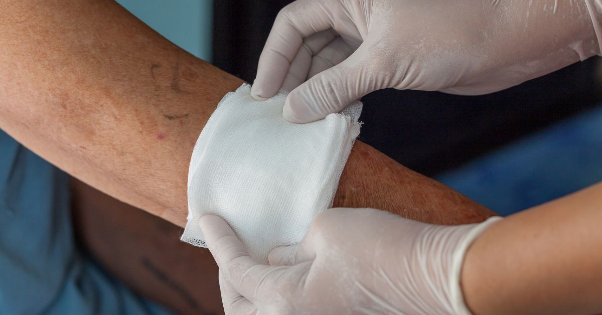 doctor wearing latex gloves holding a gauze patch over an old man's arm