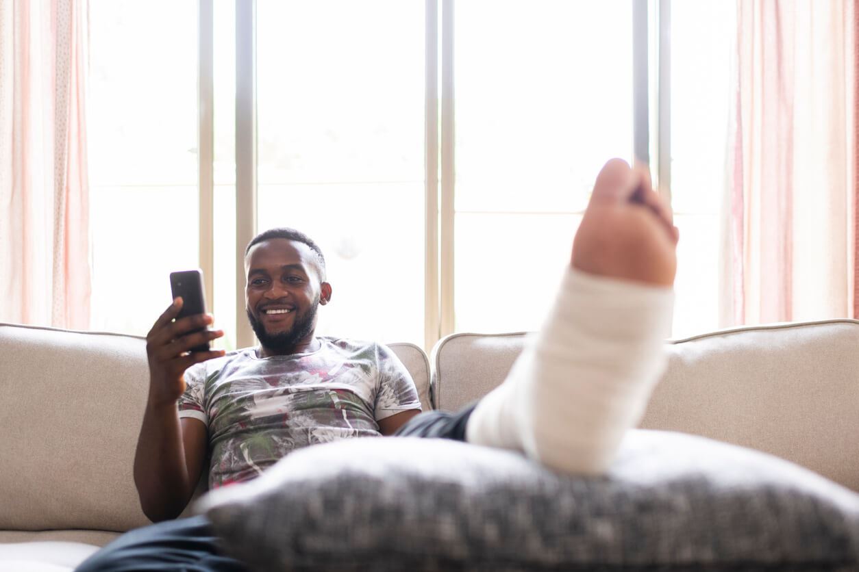 Man smiling using phone with injured foot