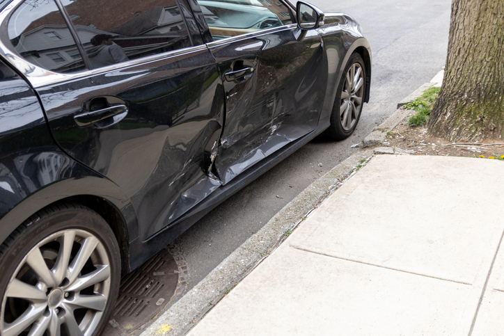 Black car with significant side damage parked on an urban street